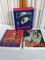 Two softcover Picasso art books and blue cardboard box with photograph of Picasso