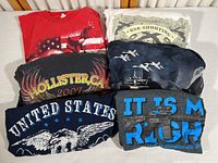 All six T-shirts folded and arranged showing the design graphics and themes of military, motorcycle, and patriotism.