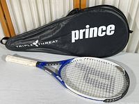 Full view of the Prince Triple Threat Cloud tennis racquet laying next to its black zippered vinyl carrying case labeled 'Prince' and 'Triple Threat'. Shows the complete racquet with white grip and blue and black frame.