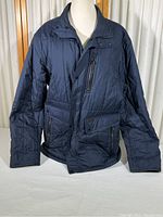Front view of navy blue insulated quilted nylon jacket on mannequin, showing zippered and snap button pockets.