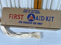 Closed cardboard first aid kit box with logo and carrying strap.