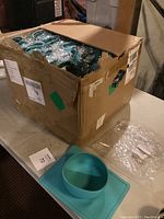 Box containing multiple sealed teal silicone placemat bowls with one bowl positioned next to the box for display.