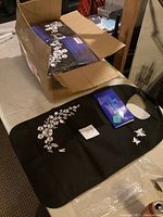 Cardboard box opened showing multiple black adult bibs/aprons inside with white floral pattern