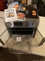 Front view of Kalorik Maxx air fryer oven with doors open showing accessories inside and manuals on top.