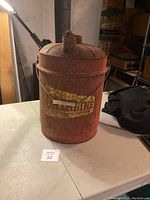 Front view of antique red metal gas can showing the faded yellow 'Gasoline' label and rusty surface.