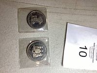 Two silver-colored collectible coins in protective plastic sleeves placed on a light surface.