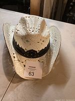 Photo of white woven straw cowboy hat with brown band taken from top front angle showing vented diamond pattern and brim