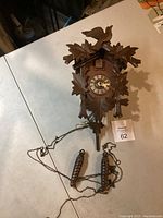 Overall view of wooden cuckoo clock lying flat, showing attached chains and pinecone weights.