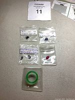 Overview of multiple small plastic bags with loose gemstones and a green jade ring on gray surface