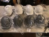8 hard hats on table, 4 white and 4 gray, all sealed in plastic.