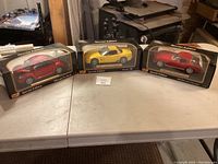 Three boxed model cars displayed on a table including a red 1965 Chevrolet Corvette, a yellow Corvette ZR1, and a red 1961 Chevrolet Corvette.