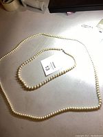 Two pearl necklaces laid flat, showing their general appearance and size difference.