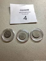 Three small silver-colored coins in protective cases with auction paper showing lot number