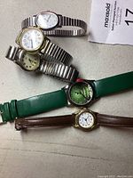 Four wristwatches laid out on a surface, showing different bands and watch face styles.