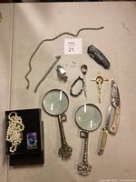 Full lot overview with all items displayed on table including necklaces, magnifying glasses, knives, and Zippo lighter.