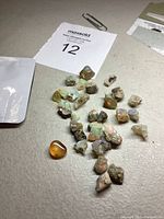 Overview of lot showing approximately 30 raw opal stones with some showing iridescent colors, plus one rounded polished stone with amber tones.
