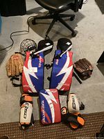 Photo of all items laid out on floor: gloves, leg and chest protectors, wrist/elbow guards, and face mask helmet