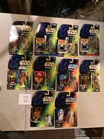 Full overview of 11 Star Wars Power of the Force action figures in original packaging arranged on a white table.