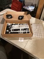 Black felt word board with white plastic letters and numbers on sprue frames inside a cardboard box, two black drawstring pouches visible on top of the box.