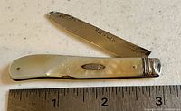 Pocket fruit cutter with blade partially open, showing wear and hallmarked sterling blade, pearl handle with oval metal inset.
