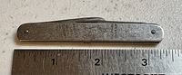 Metal folded pocket tool with Johnnie Walker logo and text engraved on one side alongside a ruler for scale