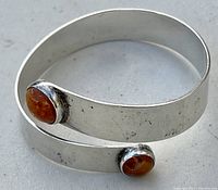 Clear image of the sterling silver open bangle bracelet showing two amber stones at the ends, placed on a white surface.
