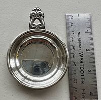 Top view of the round sterling silver wine taster next to a ruler showing approximately 2.5 inch diameter.