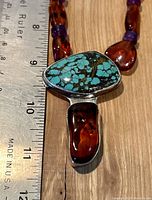 Close-up of pendant with turquoise stone and amber piece next to a ruler for size reference.