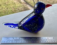Side view of cobalt blue glass bird paperweight with clear tail, placed near a ruler to show size of approx. 5.5 inches long.