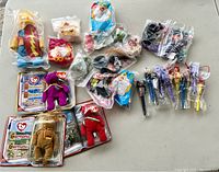Top view of vintage McDonald's Happy Meal toys, including figures in original sealed plastic packaging, assorted characters, and Ty Beanie Baby plush bears with tag cards.