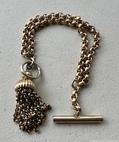 Full view of the gold-tone pocket watch chain showing the tassel end and T-bar clasp on opposite sides.