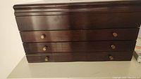 Front view of the wooden jewelry box showing four drawers with round brass knobs.