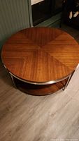 Round coffee table with wood veneer top in a radial pattern, metal trim, and visible damage on the edge.