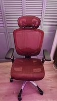 Front view of red mesh ergonomic office chair with adjustable headrest and armrests
