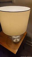 Full view of the table lamp showing white fabric shade and clear glass base