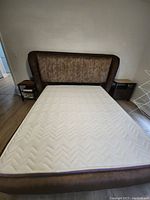 Front view of queen mattress on brown upholstered bed frame with padded headboard and visible wear