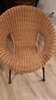 Front view of round wicker chair showing woven seat and cut-out sides with metal legs