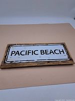 Full view of the aged "Pacific Beach" sign mounted on a rectangular weathered wooden board showing the entire lettering and framing.