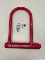 Full view of red Ming Tay U-lock with two keys laid inside the lock opening against a white surface.