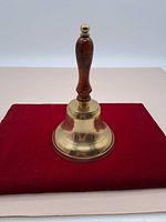 Side view of the brass hand bell showing polished brass bell and dark wooden handle with brass finial.