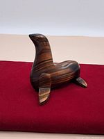 Full view of the carved wooden seal ornament positioned on a red cloth, showing overall shape and form with curved flippers and a raised head.