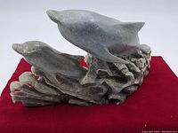Side angle showing two dolphins carved in stone with detailed wave base, placed on red cloth background.