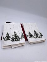 Two white towels folded showing green pine tree embroidery. The towels appear to be vintage with slight wear visible in texture.