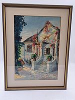 Framed watercolour painting showing a white house with stairs, vines, and potted plants in a detailed exterior scene.