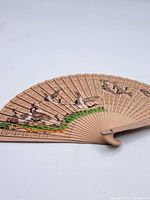 Full view of vintage wooden hand fan opened, showing bird illustrations and carved rib patterns.