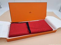 Opened orange Hermès presentation box with scarf folded inside and tissue paper on sides