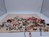 Wide view of the assortment of costume jewelry spread out on cardboard showing various bracelets, necklaces, keychains, and watches with mixed colors and materials.
