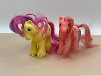 Photo showing both vintage My Little Ponies, the yellow one with pink and purple hair, next to the pink pony with long pink hair.