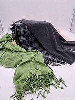 Three scarves displayed together: a green Ricki's rayon scarf with fringe, a solid dark grey scarf, and a grey plaid scarf with fringed ends.