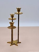 Full view of the metal candle stand showing three candle holders arranged at different heights with a star-shaped base.